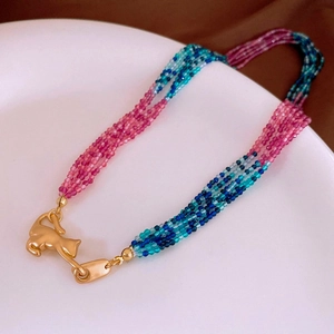 Detail of multi-layer crystal bead necklace featuring a golden cat pendant on a white plate