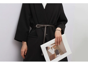 Detail of slim dark brown leather belt with knot design over a black suit blazer