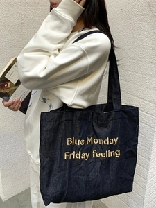 Borsa tote in denim blu scuro con ricamo dorato indossata a spalla con un outfit casual