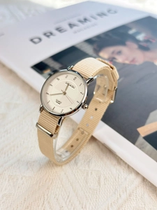 Close-up of a minimalist silver quartz watch with a beige nylon strap on a textured fabric
