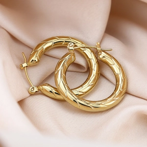 Detailed macro view of gold-plated hollow hoop earrings with wheat leaf engraving on silk