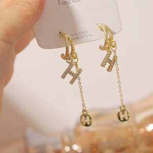 Macro detail of gold tassel earrings with rhinestone letter H charm and metal disk