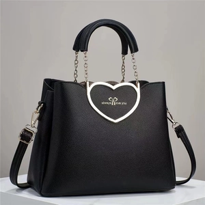 Detailed close-up of a black heart-shaped handbag featuring litchi grain texture and metal chain
