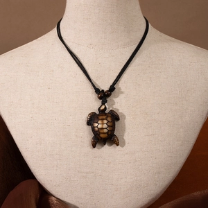 Maori style resin sea turtle pendant on black woven cord displayed on a linen mannequin