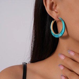 Detail view of large teal marble acrylic hoop earring with gold lining on a model