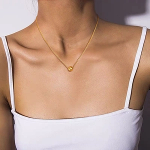Detail showing a golden necklace with a textured round bead pendant on a female model