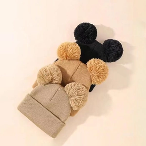 Flat lay of knit beanies in black, camel, and beige featuring double pom-pom ears