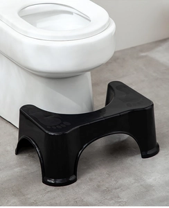 Detail of a U-shaped black plastic toilet step stool with anti-slip foot texture in bathroom