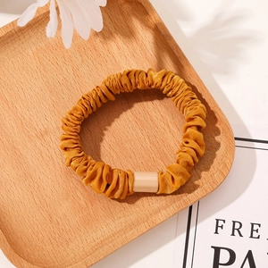 Detail of a ginger yellow satin scrunchie with a stylish rectangular resin buckle ornament