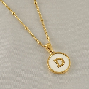 Macro detail of 18k gold bead chain necklace with round white shell letter D pendant
