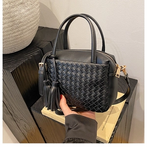 Detailed close-up of black woven leather texture and elegant tassel charm on handbag
