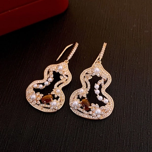 Détail de boucles d'oreilles vintage dorées avec œil de tigre, perles et zircons sur bois