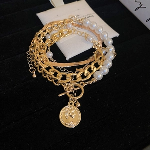 Detail of layered gold chains, pearl strand, and queen coin pendant on black velvet