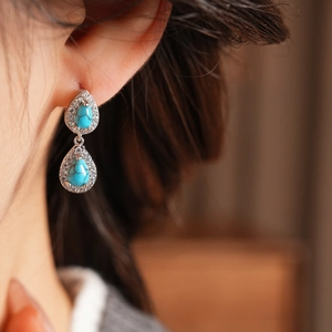 Close-up of vintage teardrop earrings with turquoise stones and cubic zirconia on model
