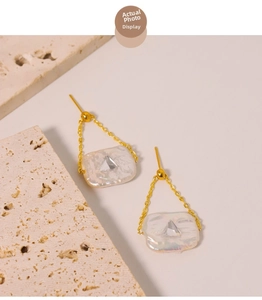 Detailed view of baroque pearl earrings with gold chain and inset triangle gemstone