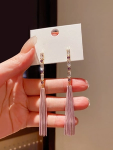 Detailed shot of long gold earrings with purple gemstones and pinkish chain tassels