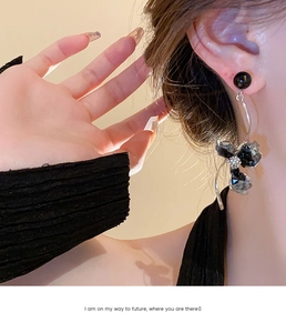 Macro detail of long silver drop earrings with black crystal bow and beaded accents