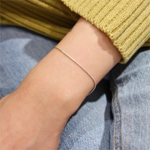 Macro view of minimalist silver snake chain bracelet worn on a wrist over casual clothing