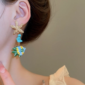 Close-up of starfish and turquoise fish drop earring worn by a model for a beach style look