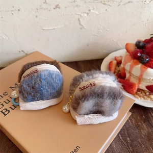 Detail of plush AirPods case with faux pearl pendant on top of a vintage book
