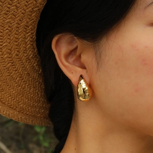 Macro view of large gold teardrop earrings with a high-polished mirror finish on a model