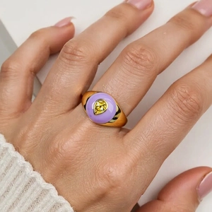 Detail of gold wide band ring with purple round gemstone and yellow teardrop zircon