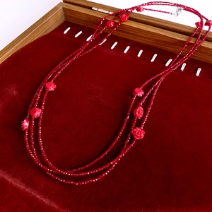 Macro shot of red beaded long necklace with small rose charms in a velvet display box