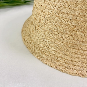 Macro shot of beige raffia bucket hat showing natural fiber texture and white stitching