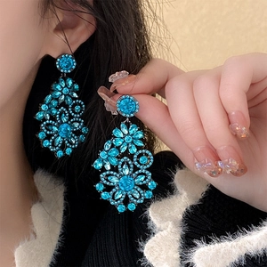 Detailed view of long blue rhinestone flower drop earrings worn by a model