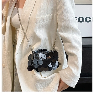 Detail of a sparkling black sequin crossbody bag with silver chain strap on a model