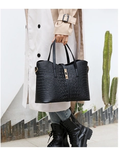 Detail of black crocodile texture tote bag with metallic turn-lock and dual top handles