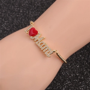 Détail du bracelet MAMA doré avec texte I Love Mom et breloque coeur rouge au poignet