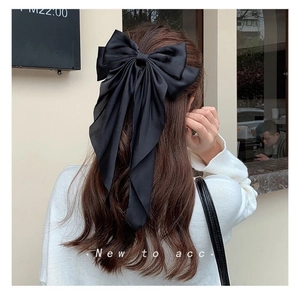 Detail of a large black satin bow hair clip with ribbons worn on the back of the head