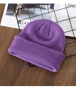 Close-up of purple knitted beanie cap laid on metal grid over dark wood surface