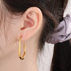 Close-up of polished gold U-shaped oval earrings worn by a model to show texture