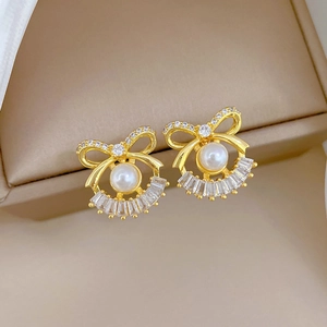 Elegant gold bow earrings with white pearls and sparkling zircons in a jewelry box