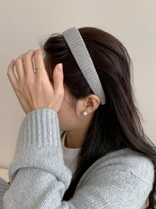 Gros plan d'un modèle portant un bandeau en tricot gris, bague dorée et perles blanches