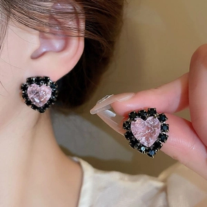 Close-up of heart-shaped pink resin earrings with black rhinestones on a metal base