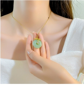 Detail view of gold titanium necklace with green faux jade pendant and crystal leaf charm