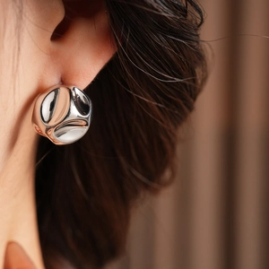 Close-up of stylish silver circular earrings with an irregular pleated metal surface