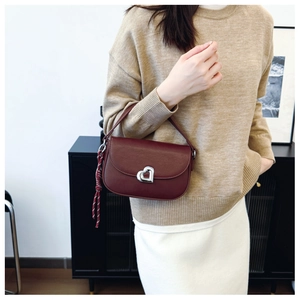 Detail of burgundy saddle bag featuring silver heart clasp and woven rope pendant