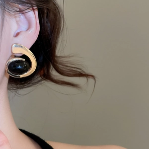 Close-up of elegant gold C-shaped earrings with black oval gemstone on a model