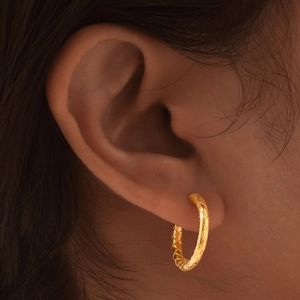 Close-up of golden hoop earrings featuring a sophisticated criss-cross quilted pattern