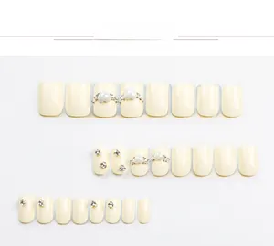 Dettaglio macro di unghie finte quadrate bianco crema con perle a cuore 3D e strass lucidi