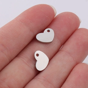 Macro shot of silver heart pendants on fingers showing precise 7.5x10mm scale and mirror finish