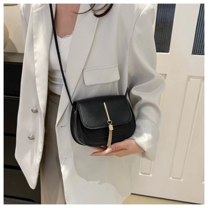 Close-up of black leather crossbody bag with long gold metal fringe on a white blazer