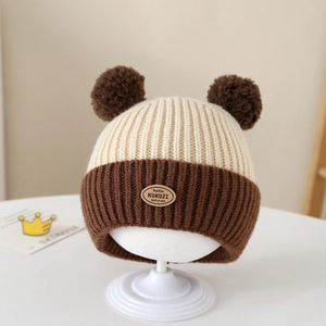 Detail of baby knit hat featuring contrast colors, dual pompoms and a leather brand patch