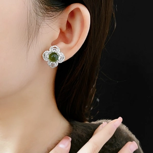 Close-up of silver four-leaf clover stud earring with green gemstone and zircon halo