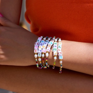Close-up of colorful beaded LOVE bracelet set worn on wrist with orange outfit