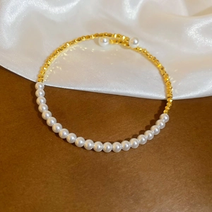 Detail of beaded bracelet with white pearls and gold faceted metal beads on white silk